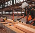 Man in orange and black vest wearing white helmet holding yellow and black power tool photo