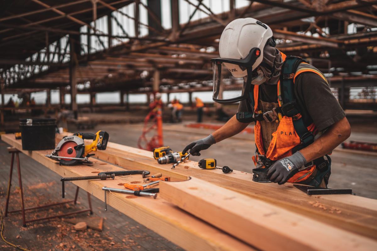 Man in orange and black vest wearing white helmet holding yellow and black power tool photo